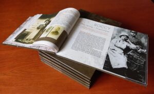Prezentacja albumu "Korzenie Siekierek": Na stercie czterech albumów stoi piąty album otwarty. Na otwartych stronach widać zdjęcia rodzinne z opisami historii rodzin siekierkowskich.