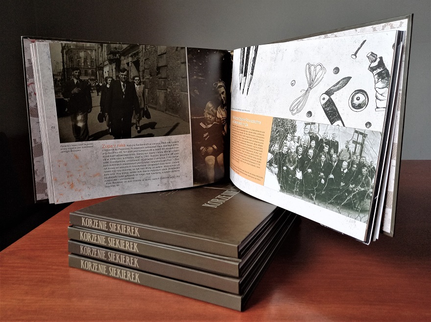 Prezentacja albumu "Korzenie Siekierek": Na stercie czterech albumów stoi piąty album otwarty. Na otwartych stronach widać stare zdjęcia rodzin skierkowskich w sepii i krótkie notki opisujące fotografie.