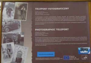 Tablica informująca o projekcie Story Savers w ramach którego w Bibliotece w Odda w Norwegii zaprezentowana została wystawa "Teleport Fotograficzny" Artura Pawłowskiego. Na brązowym tle z lewej strony nieregularnie ułożone zdjęcia z wystawy (przedstawiają człoenków rodzin sierekowskich w tych samych sceneriach i pozach po kilkudziesięciu latach np. bracia na rowerze jako dzieci i jako dorośli mężczyźni. Po prawej stronie informacja o wystawie, projkecie Story Savers i projkecie Korzenie Siekierek w języku polskim i angielskim oraz logotypy sponsorów i organizatorów przedsięwzięcia.